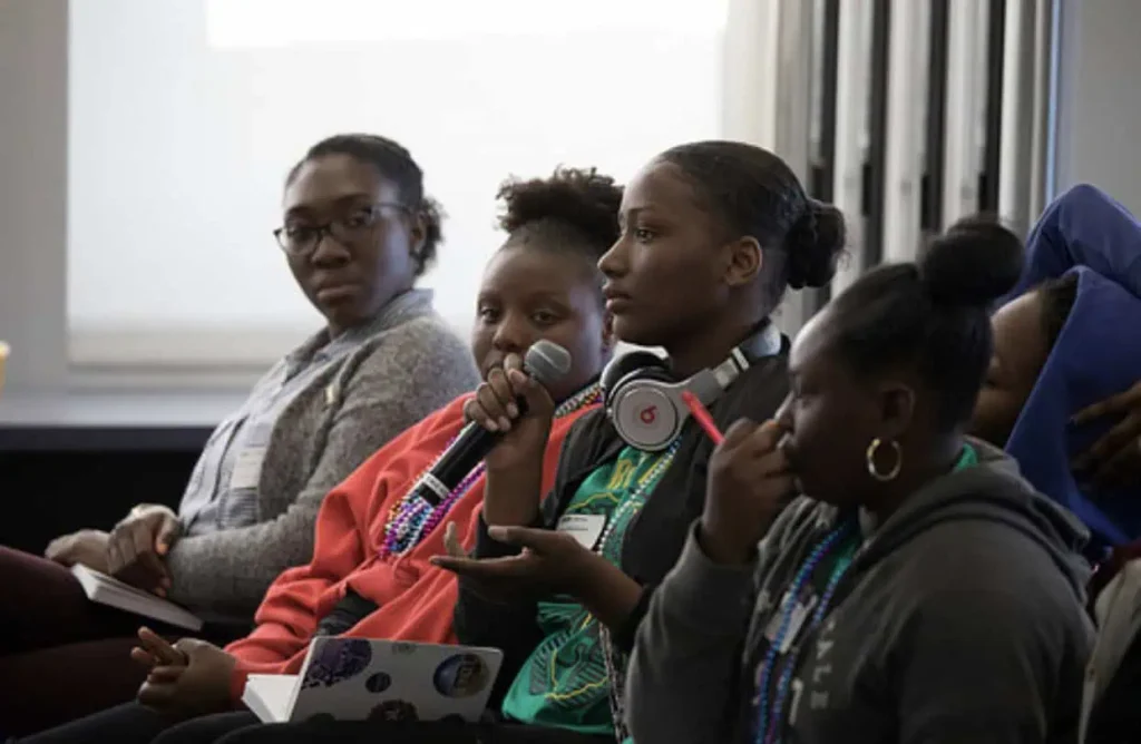 Young woman speaking into a microphone during a classroom discussion.