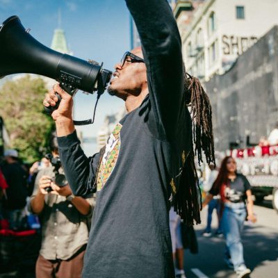 Person holding a megaphone while leading a gathering in an urban setting.